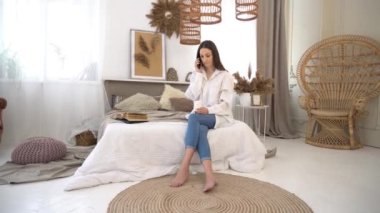 4k young woman sitting on the bed in the bedroom and enjoying a cup of coffee