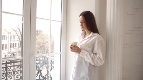 Νεαρή Γυναίκα Στέκεται Δίπλα Στο Παράθυρο Πίνοντας Από Φλιτζάνι Καφέ — Αρχείο Βίντεο
