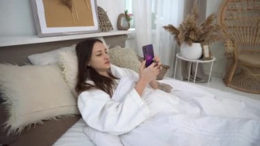 4K Güzel kadın sabah uyandıktan sonra yatakta akıllı telefon kullanıyor.