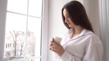 Slow Motion Woman, yatak odasının penceresinde beyaz kahve tutuyor.