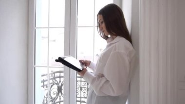 İş kadını pencerenin önünde dikilirken dijital tablet kullanıyor