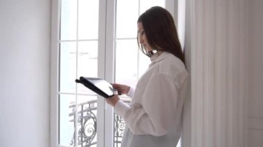 Yavaş Çekim Kadını bir pencerenin yanında dururken dijital tablette geziniyor