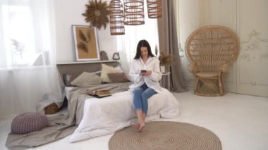 Slow Motion Young woman sitting in white bed and using a phone in her bedroom. 
