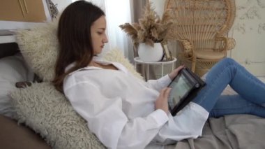 Yavaş hareket eden yatakta yatan genç kadın tablet kullanıyor.