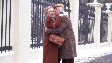 Sokakta kucaklaşan ceketli mutlu yaşlı çiftin yakın plan portresi.