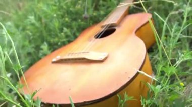 A brown acoustic guitar rests on the green grass and the morning sun.