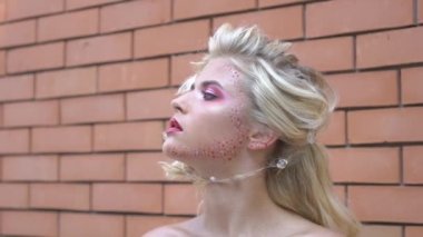 Slow Motion Stylish sweet woman with blonde hairstyle stands near brick wall