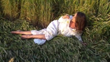 Beyaz elbiseli genç yetişkin kız Yeşil buğday tarlasında yerde yatıyor.