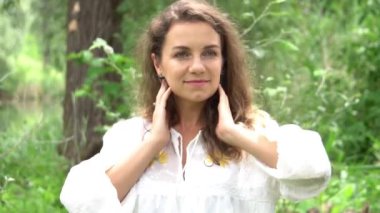 Yeşil yaz parkının arka planında beyaz elbiseli, gülümseyen genç kadın.