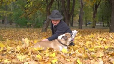 Slow Motion. Parkta köpek buldoguyla sonbahar çimlerinde oturan tatlı çocuk.
