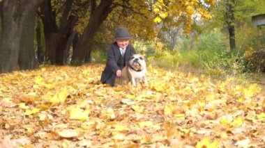 Cute Baby Boy in black suit is posing with Dog in autumn nature with bulldog