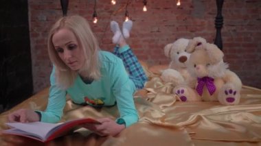 Beautiful blonde woman in home clothes on bed reading book closeup