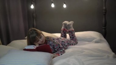 4K Cute little girl reading a book on the bed in the bedroom. 