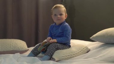 Beautiful cute caucasian baby girl reading and looking the book in a bed.