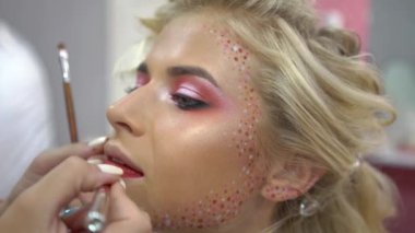 4k A young beautiful girl model master makeup artist puts a bright red lipstick