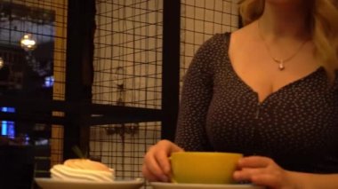 4K Genç sarışın kadın akşam bir kafe restoranında kek yiyor. 