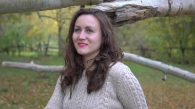 Mutlu gülen kadın güneşli bir sonbahar gününde ağaçta oturuyor.