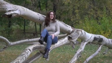 Güzel kadın, sonbahar yapraklarıyla parktaki ağaçta oturuyor..