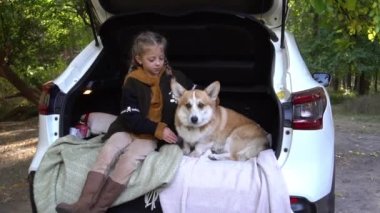 Slow Motion Girl sitting with a dog in the trunk of a car in the fall. 