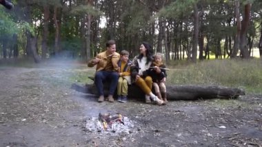 Mutlu aile kamp ateşinin yanındaki ormanda piknik yapıyor.