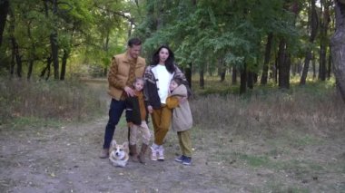 Sonbahar parkında Corgi ile altın yaprakların keyfini çıkaran dört kişilik bir aile.