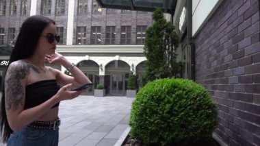 Siyah gözlüklü genç kız ve sokakta telefon tuğla desenli.