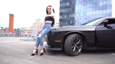 Young woman with long straight hair standing and posing near black sport car