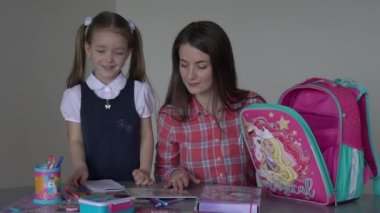 Mother and cute little daughter sitting at table and doing homework together 