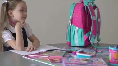 Caucasian girl sitting at the desk and writing in a notebook and doing homework.