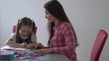 Happy child and adult are sitting at desk. Girl doing homework or education.