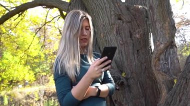 Slow Motion Girl typing message on smart phone in park on autumn day.