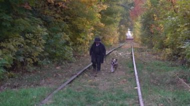 Siyah takım elbiseli küçük bir çocuk köpeğiyle parkta buldog oynuyor.