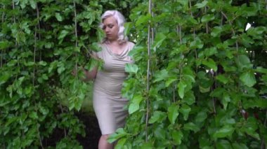 Slow Motion Caucasian woman near leaves wall, wearing dress.