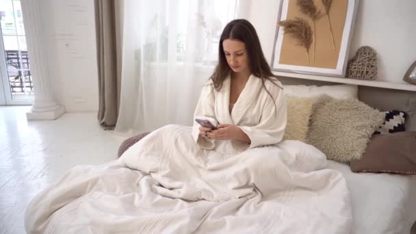 Beautiful Young Woman Using Mobile Phone Lying Bed Modern Interior — Vídeo de Stock