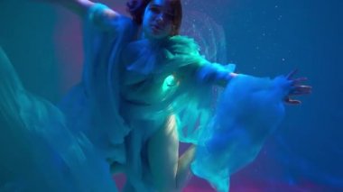 Slow Motion A girl with long dark hair swims underwater in a dress 