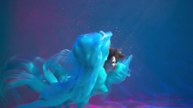 A woman with blond hair in a white dress swims underwater as if flying