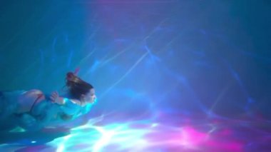 Girl shows the performance under the water, she dances in a white dress.