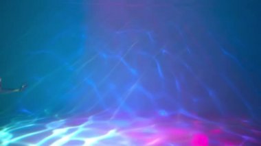 Slow Motion. Uzun siyah saçlı bir kız su altında yüzüyor.