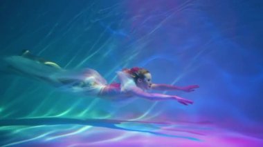 Girl swims underwater like a free diver in a white dress with beautiful fabric