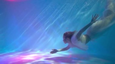 A woman, a fashion model in the water in a beautiful dress swims like a fish.