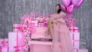 Beautiful woman in a burgundy dress-cloud, with a long train sitting on piano