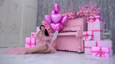 Beautiful sexy young brunette woman wearing pink evening red dress near piano.