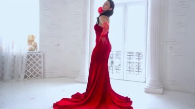 Slow Motion woman with perfect makeup and red long dress, posing near window
