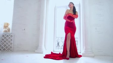 Slow Motion caucasian woman in long red train dress standing by the window