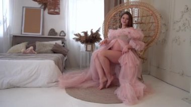 Slow Motion. Pembe elbiseli hamile kadın. Lüks beyaz odada poz veriyor.