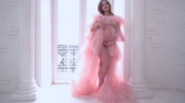 Slow Motion pregnant woman in pink dress in a white room