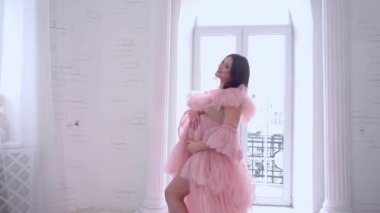 Beautiful pregnant woman in light flying peignoir dress in white interior