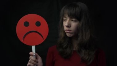 4k young woman holding sad emoticon on black background