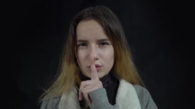 4k Young girl on black background keeping a secret or asking for silence