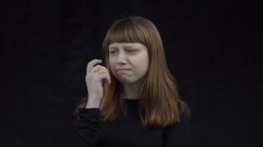 A curious girl stands against the black background and thinks